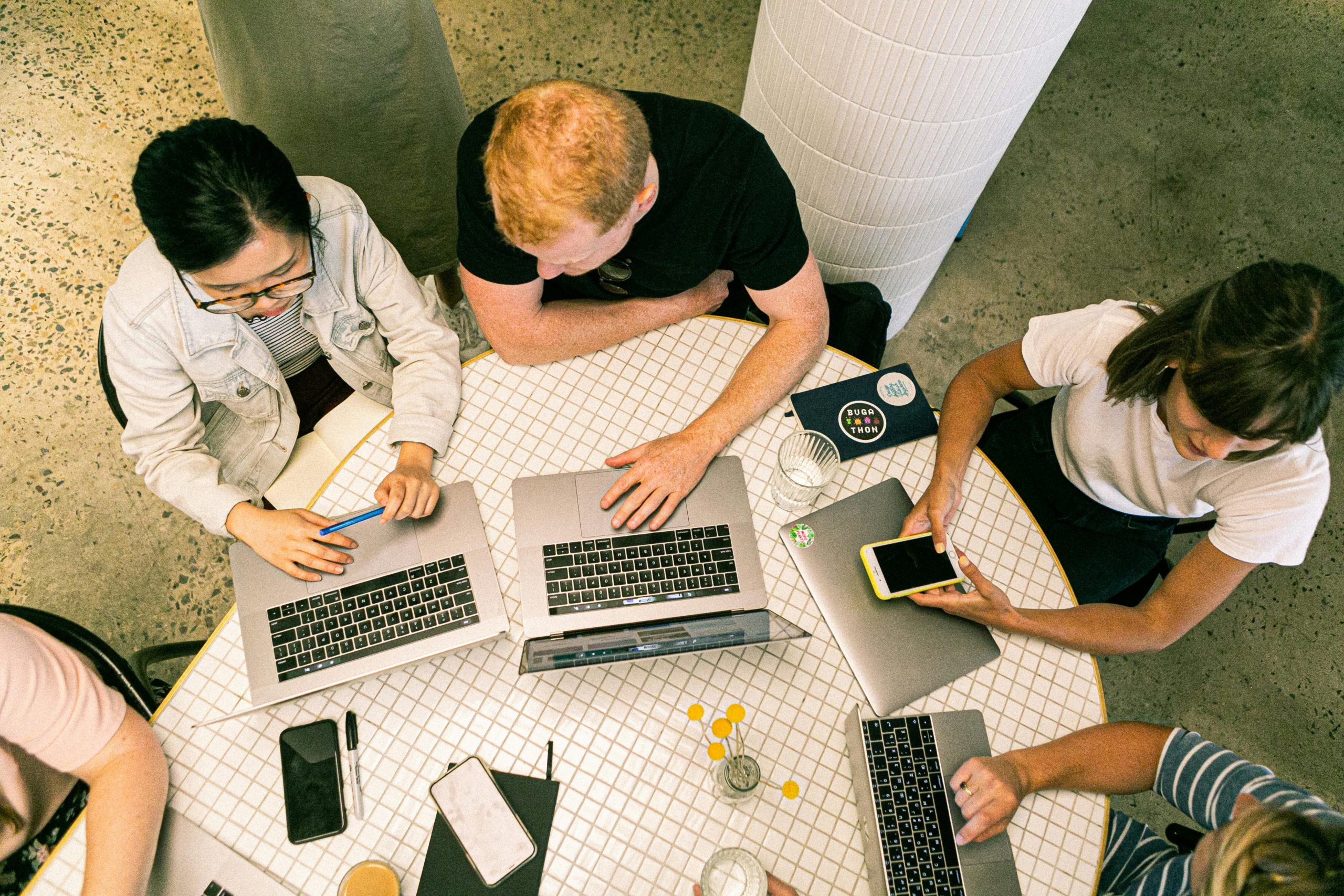 a group of people sitting around a table with laptops